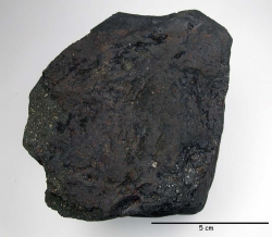 La météorite de Paris. Notez la fine pellicule noire (« croûte de fusion ») qui recouvre presque toute la pierre dont l’intérieur, parsemé de petits points blancs, n’est visible que par endroits.
